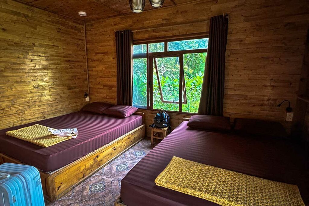 Eenvoudige houten kamer in een traditionele Tay-homestay in Ha Giang, met uitzicht op tropische natuur.