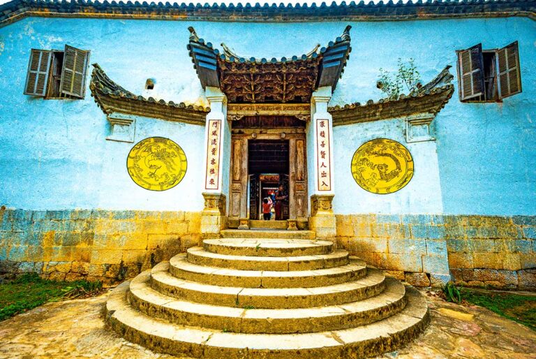 Hoofdingang van het Hmong King Palace met stenen trappen, houten poort en traditionele decoraties.