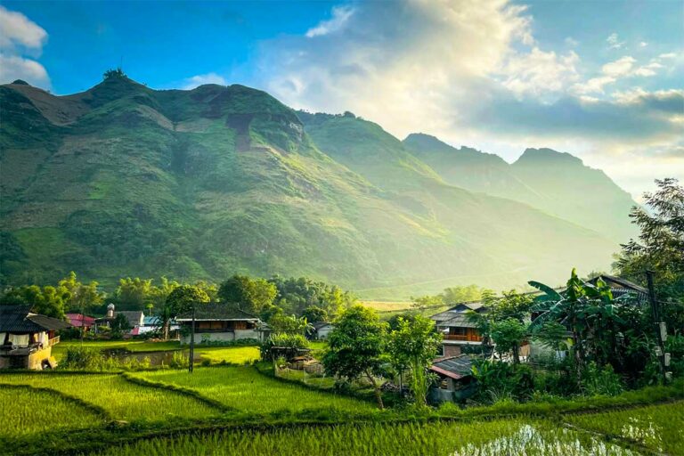 Green rice fields and wooden houses in Du Già valley with morning light on the surrounding mountains.