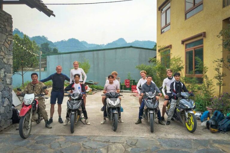 Een familie op de Ha Giang Loop Easy Rider tour staat klaar bij de motorbikes voor vertrek, met groene heuvels en een lodge-omgeving op de achtergrond.