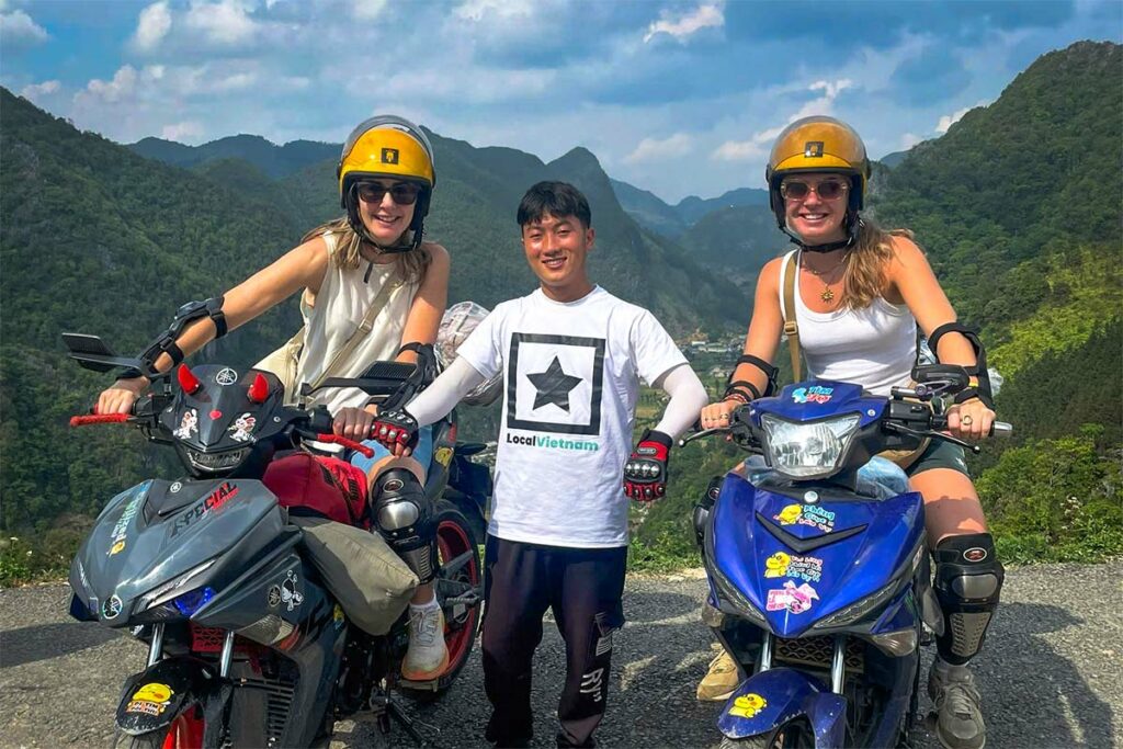Reizigers poseren met hun Local Vietnam-gids tijdens een Ha Giang Loop Easy Rider tour, met mistige bergpieken en een steile vallei op de achtergrond.