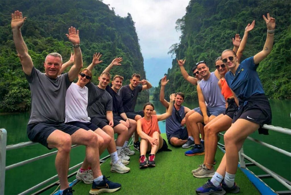 Reizigers genieten van een boottocht tijdens de Ha Giang Loop groepstour, varend tussen hoge groene karstbergen op helder turquoise water.