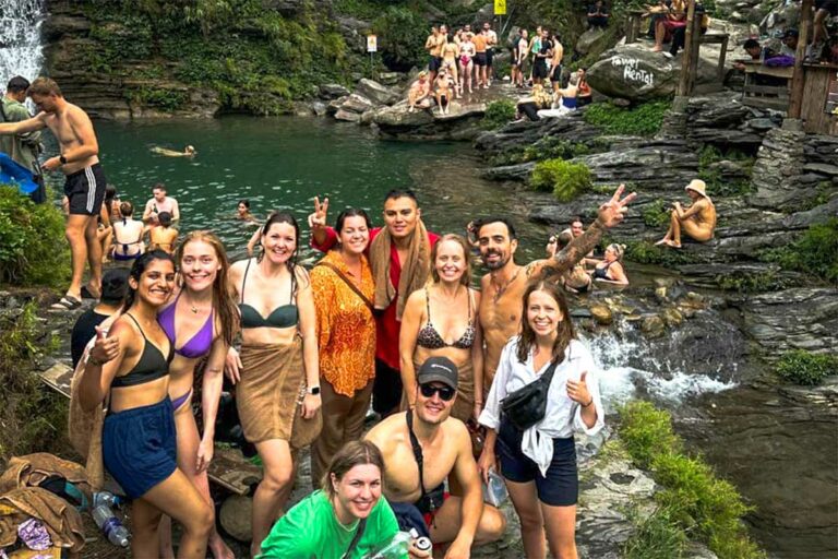 Een groep reizigers poseert bij de Du Gia-waterval tijdens de Ha Giang Loop groepstour, met zwempoelen, rotsen en andere badgasten op de achtergrond.