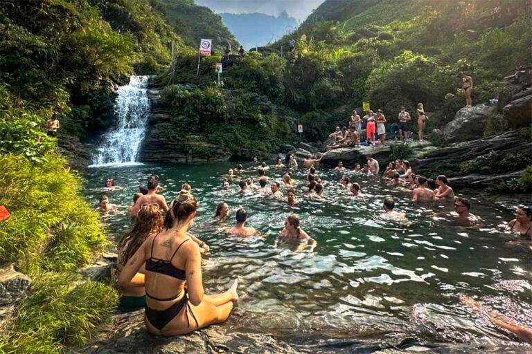 Reizigers zwemmen en ontspannen bij de Du Gia-waterval tijdens de Ha Giang Loop groepstour, omringd door rotsen, groen en stromend helder water.