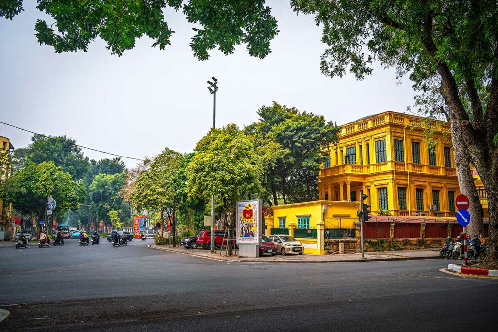 Brede straat in de Franse wijk (French Quarter) van Hanoi met geel koloniaal gebouw en veel groen