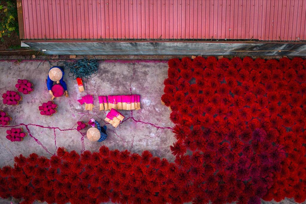 Dronefoto van Quang Phu Cau wierookdorp met geometrische patronen van rode wierookstokjes die buiten liggen te drogen.
