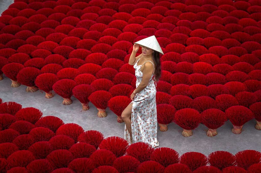Bezoeker poseert tussen rijen rode wierookstokjes in Quang Phu Cau wierookdorp, een populaire plek voor fotografie bij Hanoi.