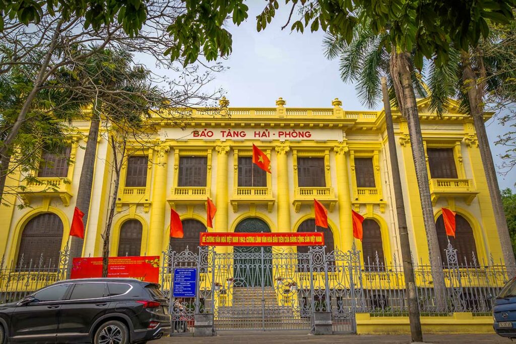 Hai Phong City Museum in een Frans koloniaal gebouw met gele façade en nationale vlaggen