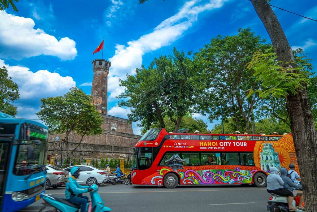 Hanoi Flag Tower gezien vanaf Lenin Park, met druk verkeer en een rode hop-on hop-off stadsbus op de voorgrond