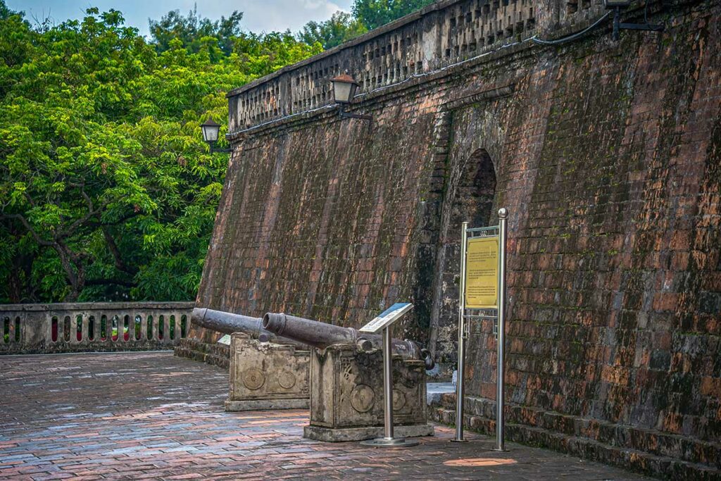 Detail van een boogvormige ingang in de muur van de Hanoi Flag Tower, met bakstenen constructie en informatiebord