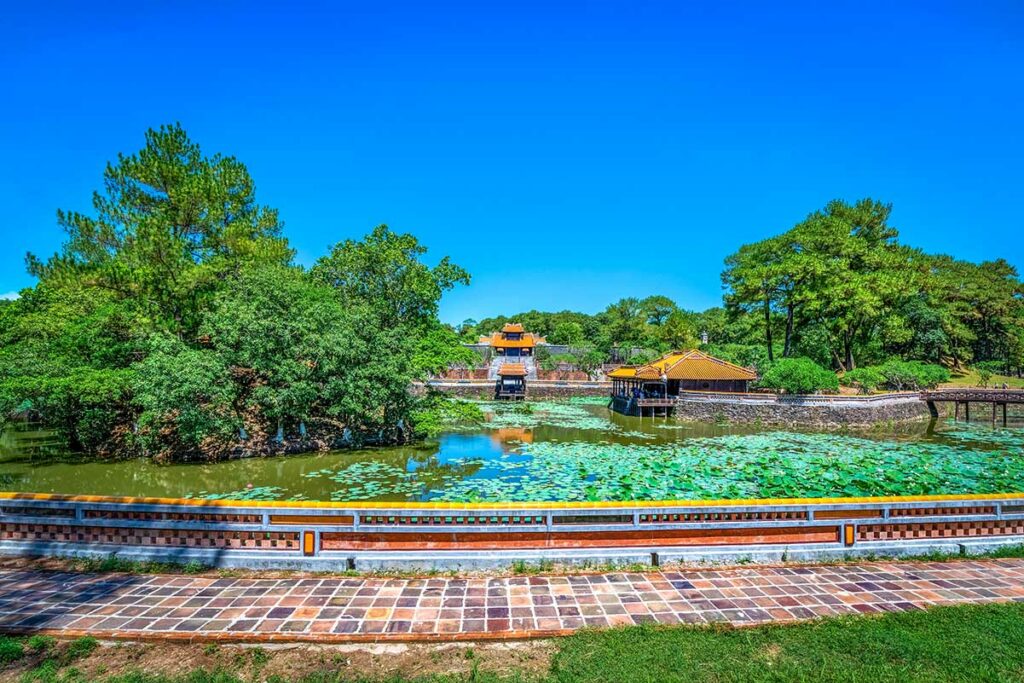 Panoramisch uitzicht over het Luu Khiem-meer bij de tombe van keizer Tu Duc, met lotusbladeren, paviljoens en paleisgebouwen langs het water.