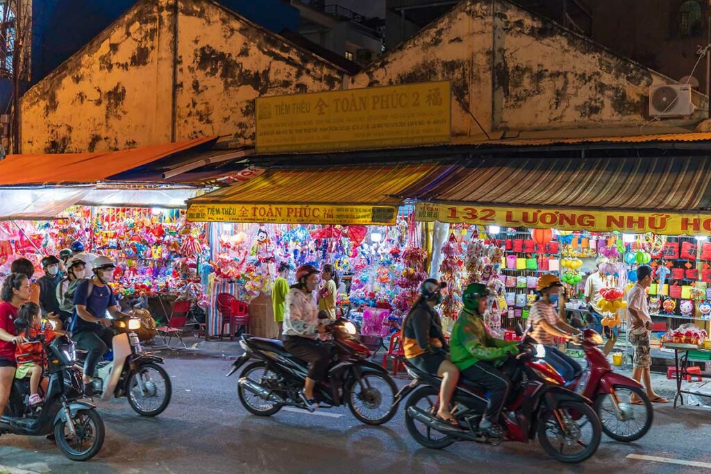 Avondbeeld van Lantern Street in Cho Lon, met winkels vol Chinese lantaarns en scooters die door de straat rijden.