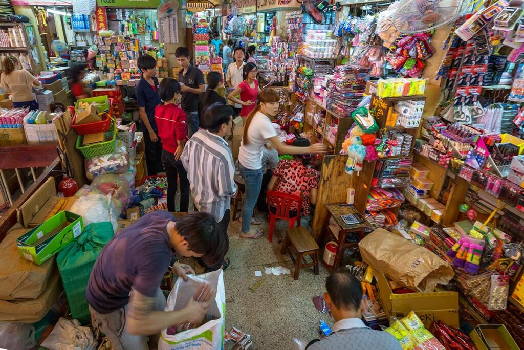 Drukke gang binnen Binh Tay Market waar lokale bewoners winkelen bij kleine kraampjes met alledaagse goederen in Chinatown, Ho Chi Minh City.