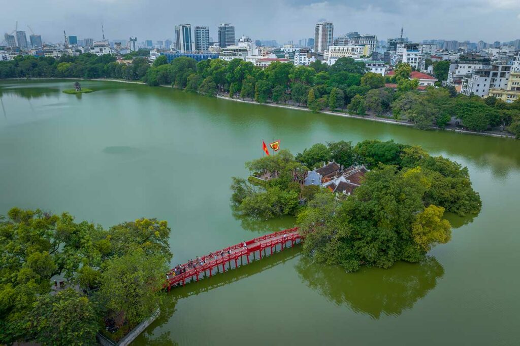 Luchtfoto van de Ngoc Son-tempel op een klein eiland in Hoan Kiem Lake, met de rode Huc-brug en de skyline van Hanoi op de achtergrond