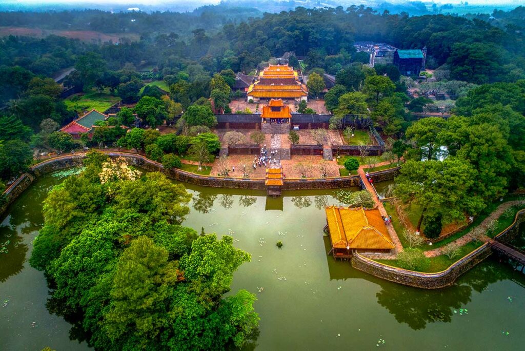 Luchtfoto van de tombe van keizer Tu Duc in Hue, met de centrale as, meren, paviljoens en paleizen die harmonieus in het groene landschap zijn aangelegd.