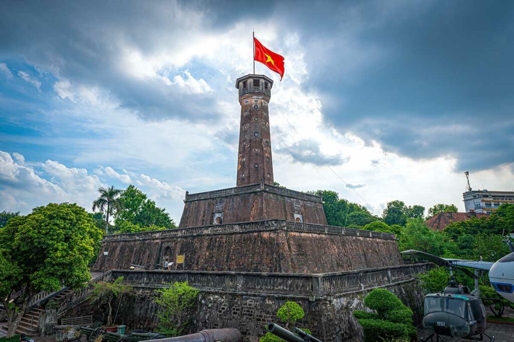 De gelaagde stenen basis van de Hanoi Flag Tower met de Vietnamese vlag bovenop, gefotografeerd vanaf de binnenplaats