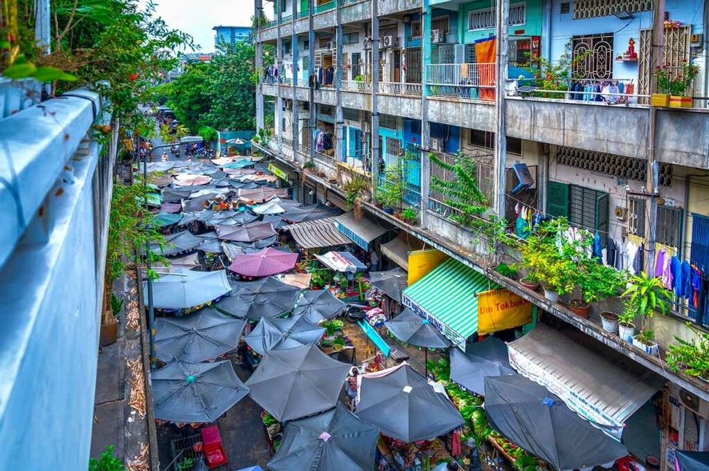 Bovenaanzicht van Phung Hung Street in Chinatown Ho Chi Minh City, met een lokale markt onder parasols en woonblokken langs de straat.