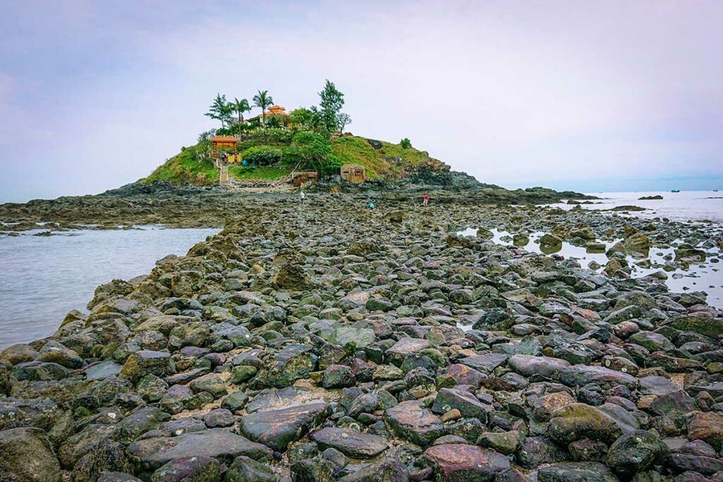 Stenen pad dat bij eb zichtbaar wordt richting Hon Ba-eiland bij Vung Tau, met de kleine tempel op de achtergrond