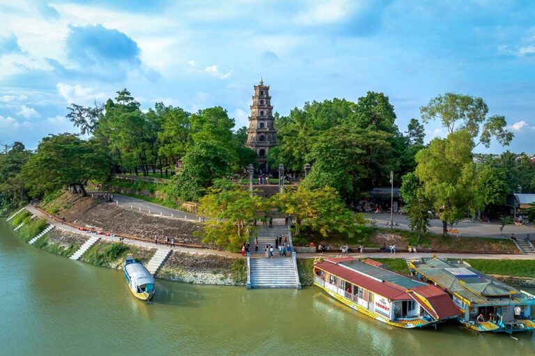 Aankomst per drakenboot bij Thien Mu Pagoda aan de Parfumrivier in Hue, met de pagodetoren zichtbaar boven de bomen.
