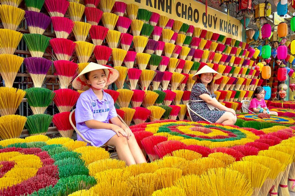 Vrouwen zitten tussen felgekleurde wierookstokjes in Thuy Xuan wierookdorp bij Hue, met bundels wierook uitgestald voor bezoekers.