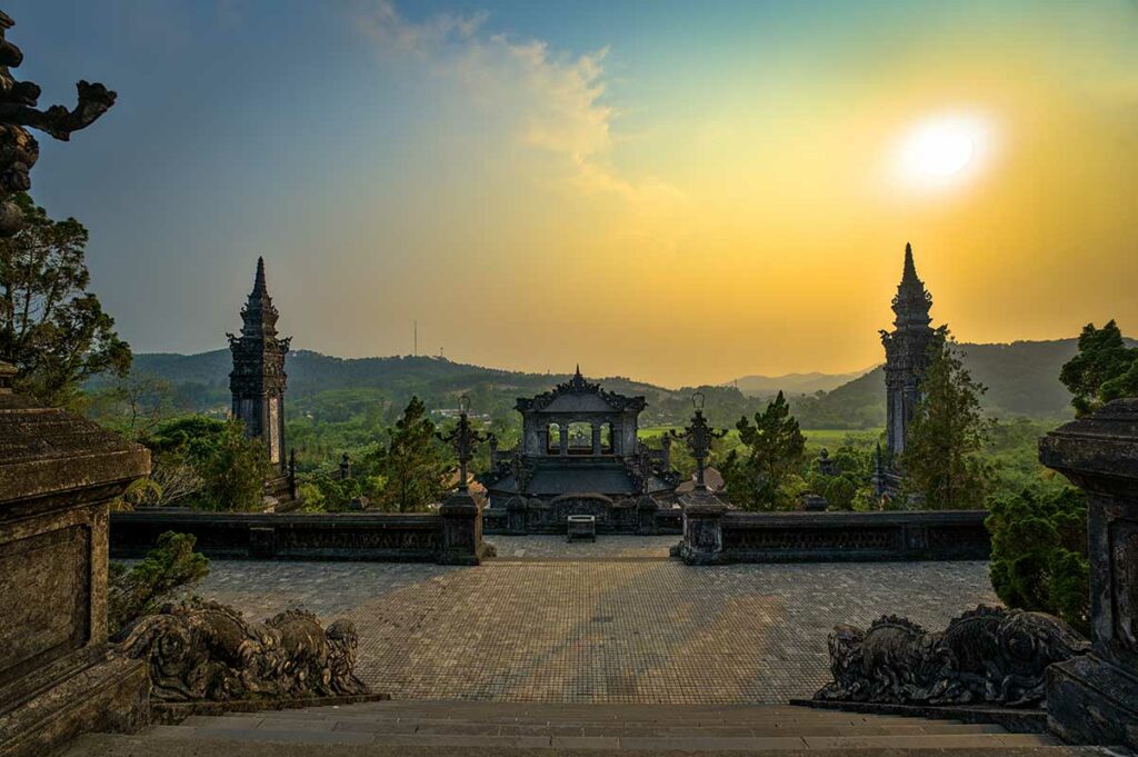 Uitzicht vanaf het bovenste terras van de Tombe van Khai Dinh in Hue, met zicht op de omliggende heuvels en het platteland tijdens zonsondergang.