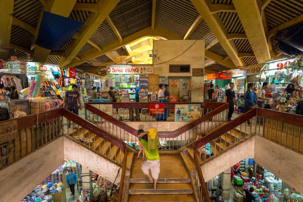 Binnen in Binh Tay Market in Ho Chi Minh City, met trappen tussen de verdiepingen en kraampjes vol huishoudelijke en dagelijkse producten.