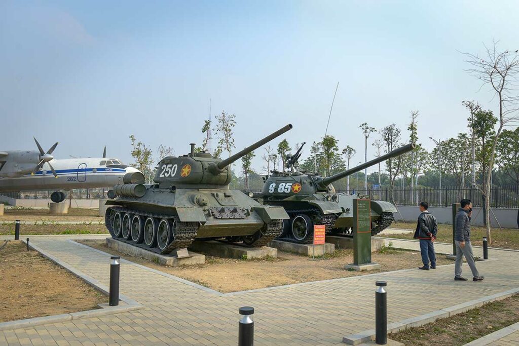 T-34 en T-54 tanks opgesteld in het buitenterrein van het Vietnam Military History Museum in Hanoi, met bezoekers op de achtergrond.