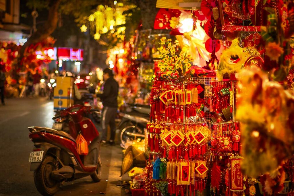 Straatverkoop en feestdecoraties in Hanoi tijdens Tet, het Vietnamese nieuwjaar, met rode versieringen en druk avondleven