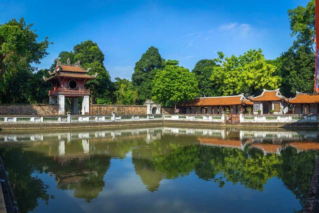 Vijver met weerspiegeling van tempelgebouwen in de Temple of Literature in Hanoi, omgeven door groene tuinen
