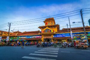 Voorkant van Binh Tay Market in Chinatown (Cho Lon) in Ho Chi Minh City, met de karakteristieke gele gevel en druk verkeer voor de markt.