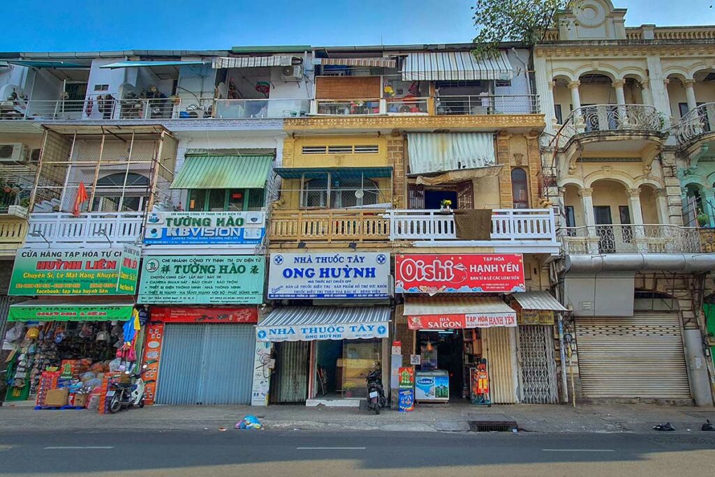 Rij oude winkelpanden in Chinatown Ho Chi Minh City met Vietnamese en Chinese uithangborden, kleine winkels en gesloten rolluiken.