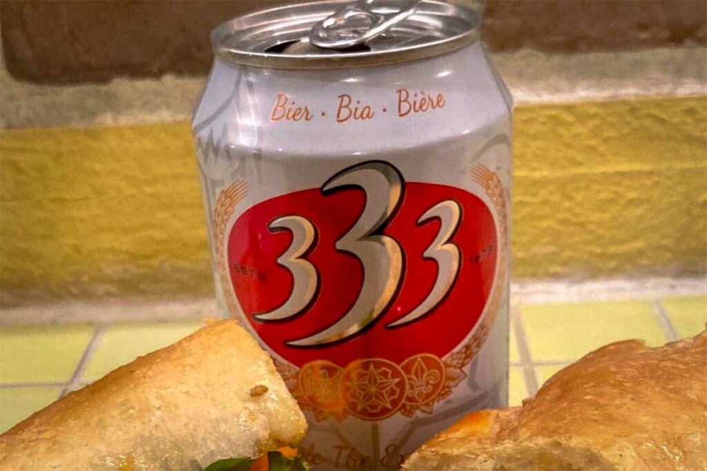 Blikje 333 bier naast Vietnamese snacks op tafel, een bekend lokaal lagerbier met een iets vollere smaak dat vaak bij maaltijden wordt gedronken