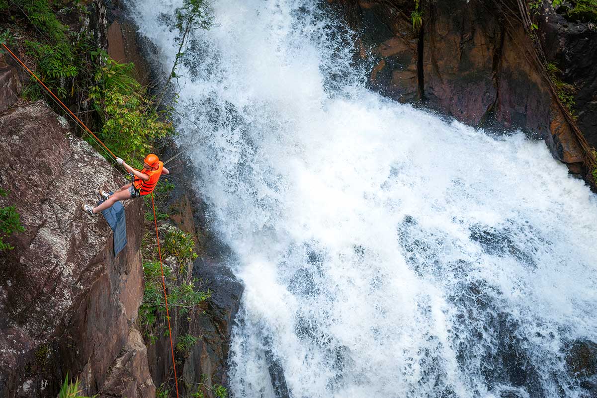 Canyoning deelnemer abseilt langs een waterval in Dalat met snelstromend water en natte rotswanden in een natuurlijke jungleomgeving
