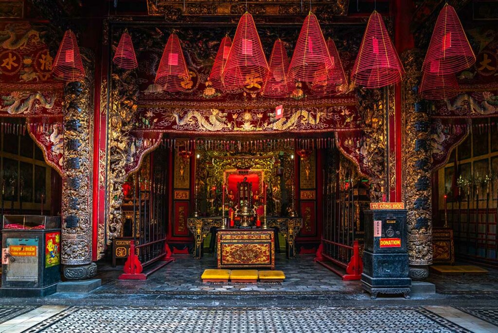 Altaar in Kien An Cung Pagoda in Sa Dec met rode wierookspiralen, rijk houtsnijwerk en vergulde details in Chinees-Vietnamese tempelinterieur