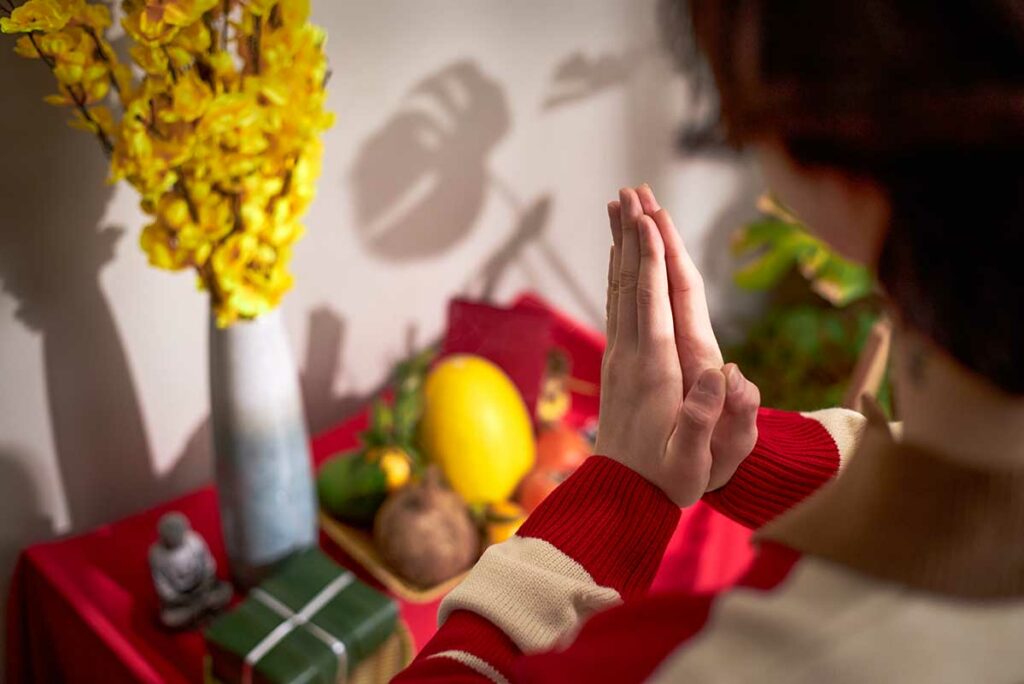 Persoon die bidt bij een huisaltaar met fruit en bloemen, een dagelijks ritueel van voorouderverering binnen de Vietnamese volksreligie