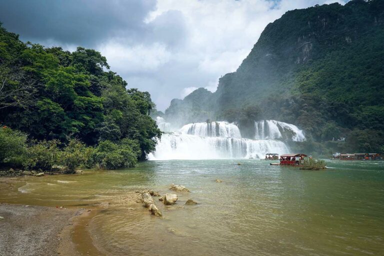 Uitzicht op de Ban Gioc Waterval in Cao Bang, met krachtige watervallen, mistige nevel en bootjes op de rivier aan de grens tussen Vietnam en China