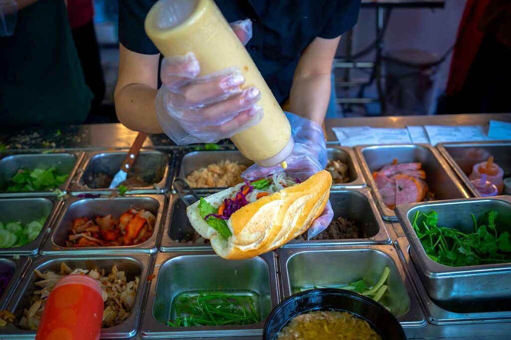 Verse bánh mì wordt belegd bij een straatkraam in Vietnam, een typisch Vietnamees broodje op basis van Frans stokbrood uit de koloniale periode.