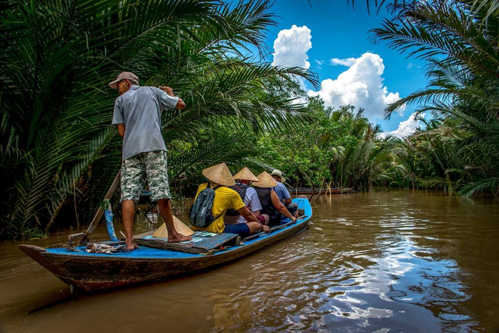 Reizigers varen per sampan roeiboot door smalle waterwegen in Ben Tre, Mekong Delta, omringd door dicht palmblad – sampan Mekong Delta