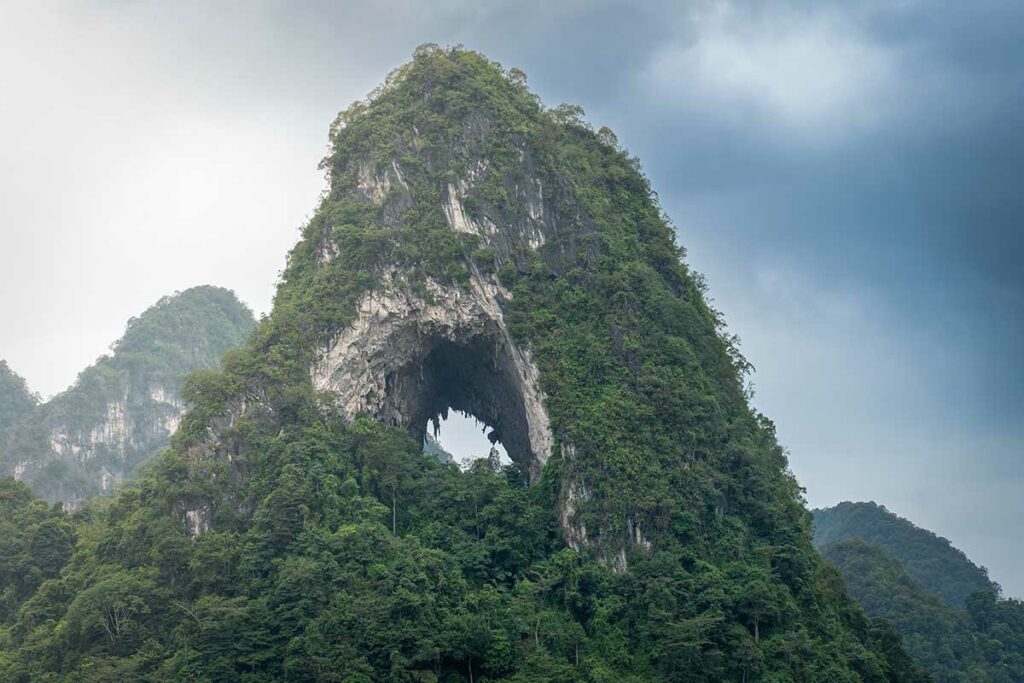 Close-up van de kalkstenen bergwand van Angel Eye Mountain met het opvallende ronde gat, begroeid met dichte vegetatie.