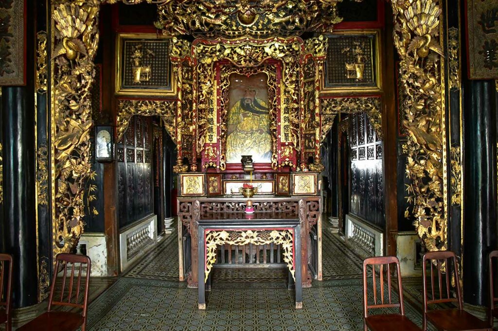 Interieur van Huynh Thuy Le Ancient House in Sa Dec met rijk versierde houten panelen, altaar en historische tegelvloer