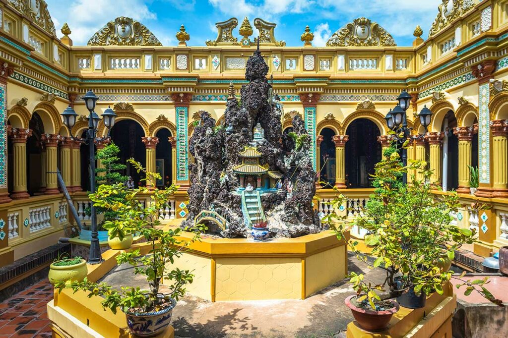 Binnenplaats van de hoofdtempel van Vinh Trang Pagoda met Europese bogen, gele gevels en centrale rotstuin