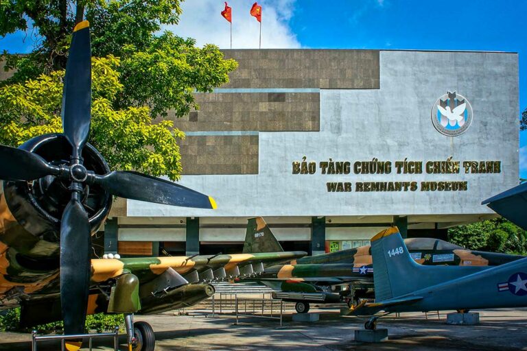 Buitenzijde van het War Remnants Museum in Ho Chi Minh City met tentoongestelde Amerikaanse gevechtsvliegtuigen en helikopters uit de Vietnamoorlog op het museumplein.