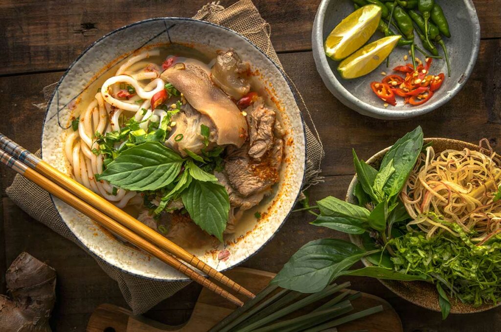 Bún bò Huế, Vietnamees noedelgerecht met dikke rijstnoedels, rund- en varkensvlees, verse kruiden en pittige bouillon, geserveerd met chili en citroen
