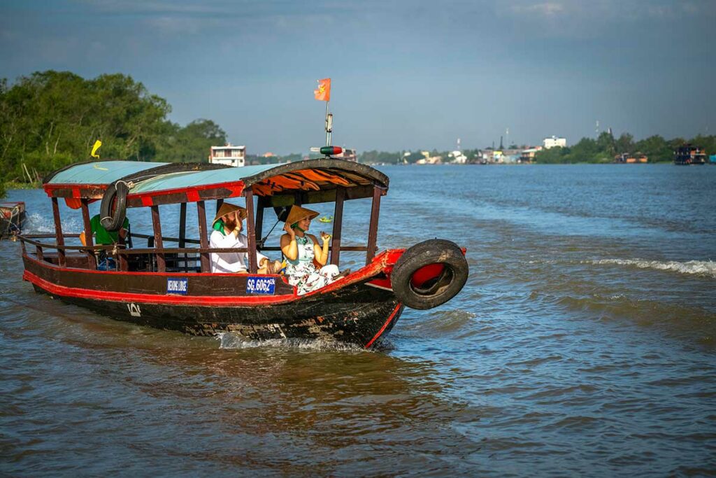 Traditionele houten boot met reizigers op de rivier bij Cai Be in de Mekong Delta met dorpen en groen landschap op de achtergrond