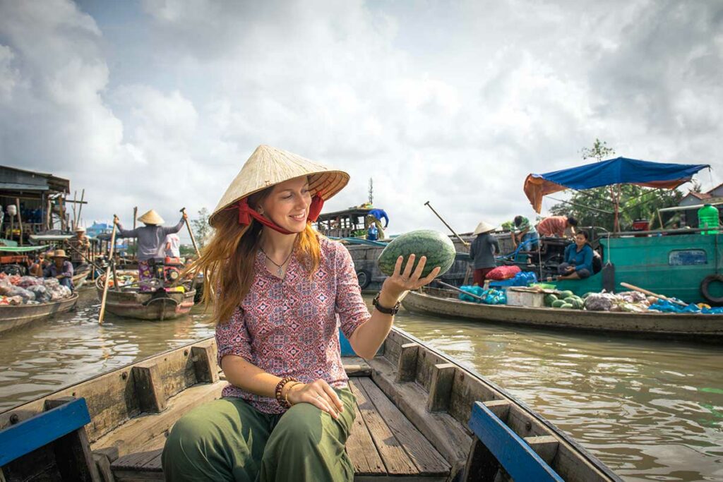 Reiziger bezoekt de drijvende markt van Cai Rang in de Mekong Delta, zittend in een houten boot tussen handelaren die fruit en groenten verkopen vanaf hun boten