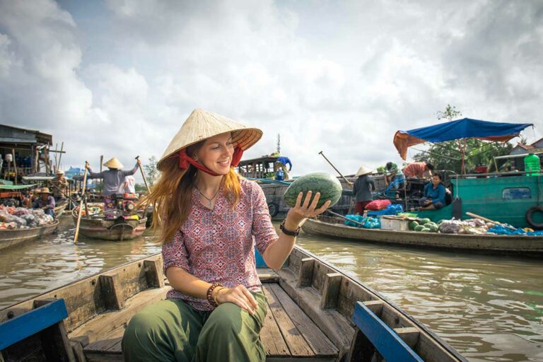 Reiziger bezoekt de drijvende markt van Cai Rang in de Mekong Delta, zittend in een houten boot tussen handelaren die fruit en groenten verkopen vanaf hun boten