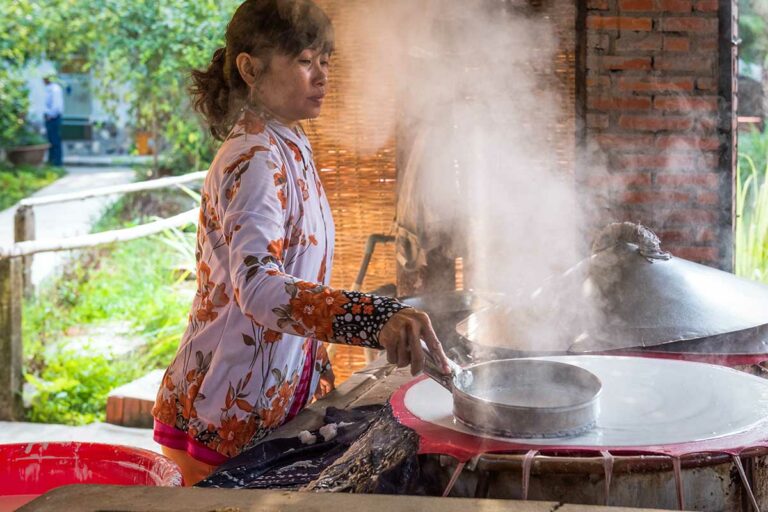 Lokale vrouw die rijstpapier maakt in Can Tho, waarbij rijstbeslag wordt gestoomd en verwerkt volgens traditionele methodes in de Mekong Delta