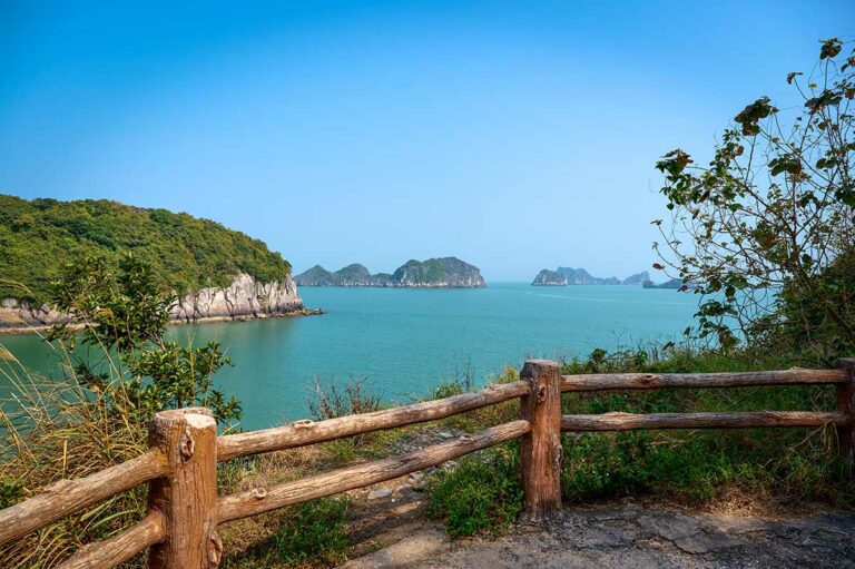 Uitzicht over de zee en kalkstenen eilanden vanaf het kustpad op Cat Ba Island, met houten hekwerk en panoramische vergezichten over Lan Ha Bay