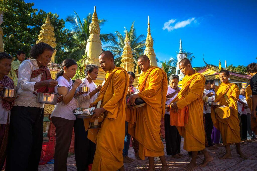 Khmer monniken in saffraankleurige gewaden ontvangen aalmoezen bij tempel in Chau Doc Mekongdelta