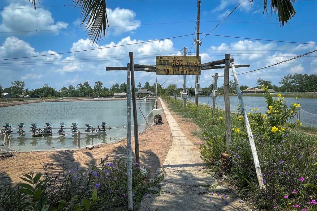 Toegang tot een homestay op Con Chim-eiland in Tra Vinh met garnalenvijvers en smal pad door het landelijke landschap